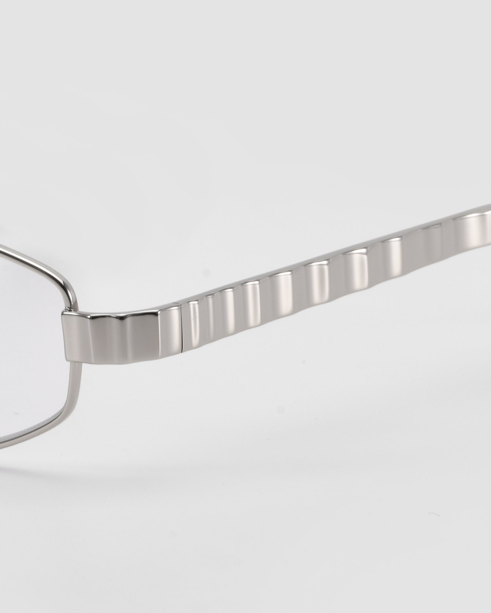 Close-up of For Art's Sake® Iris frames featuring sculptural metal with a textured, grooved temple arm, set against a plain light gray background.