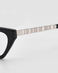 Close-up of For Art's Sake® Lavender optical frames showcasing sculptural black cat-eye acetate design with metallic ridged temple arm against a light gray background.