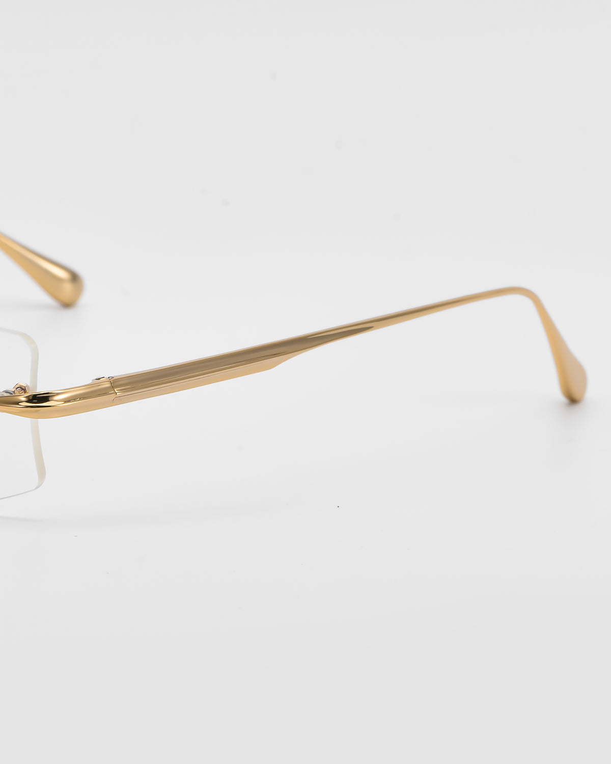 Close-up of Suri II by For Art’s Sake®: gold-rimmed optical frames with jade nose pads, showing part of the lens and temple arm against a white background.