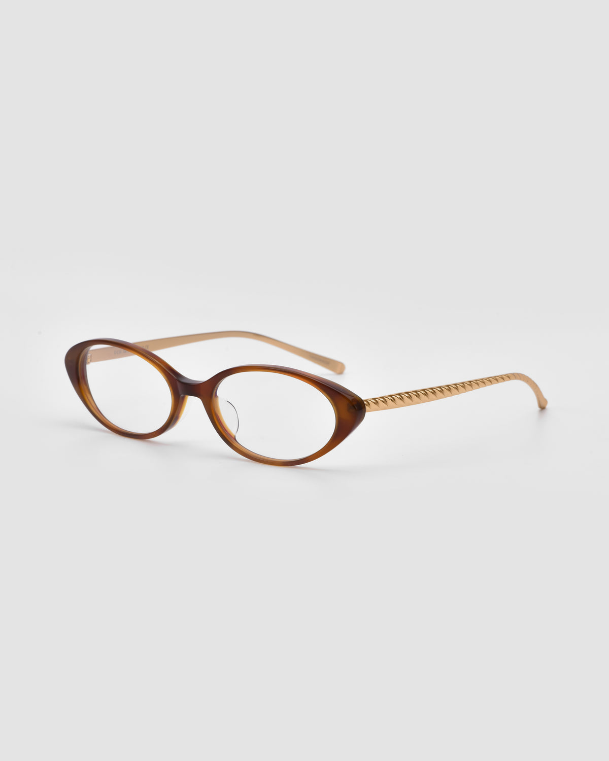 The Lumi II by For Art’s Sake® are brown oval acetate glasses with thick frames and patterned arms, shown on a plain light background.