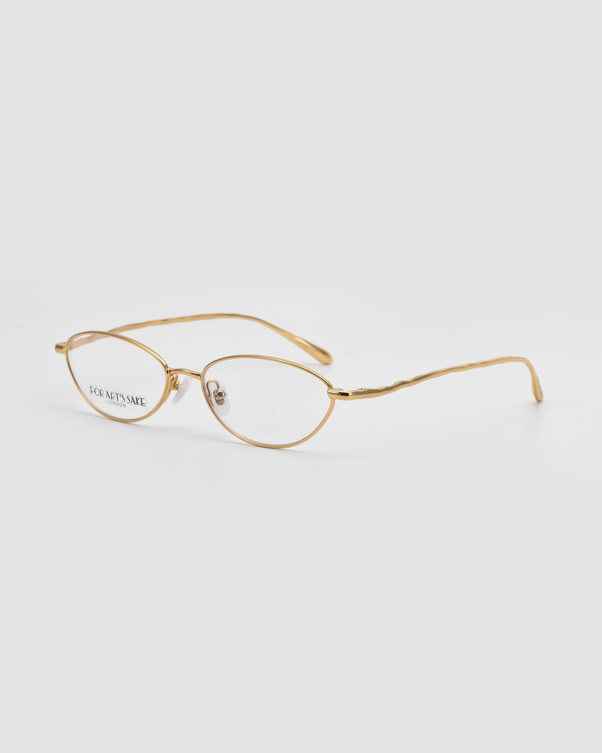Suree II by For Art’s Sake®: gold metal optical frames with an oval silhouette, clear nose pads, and gently curved temples, shown on a plain white background.
