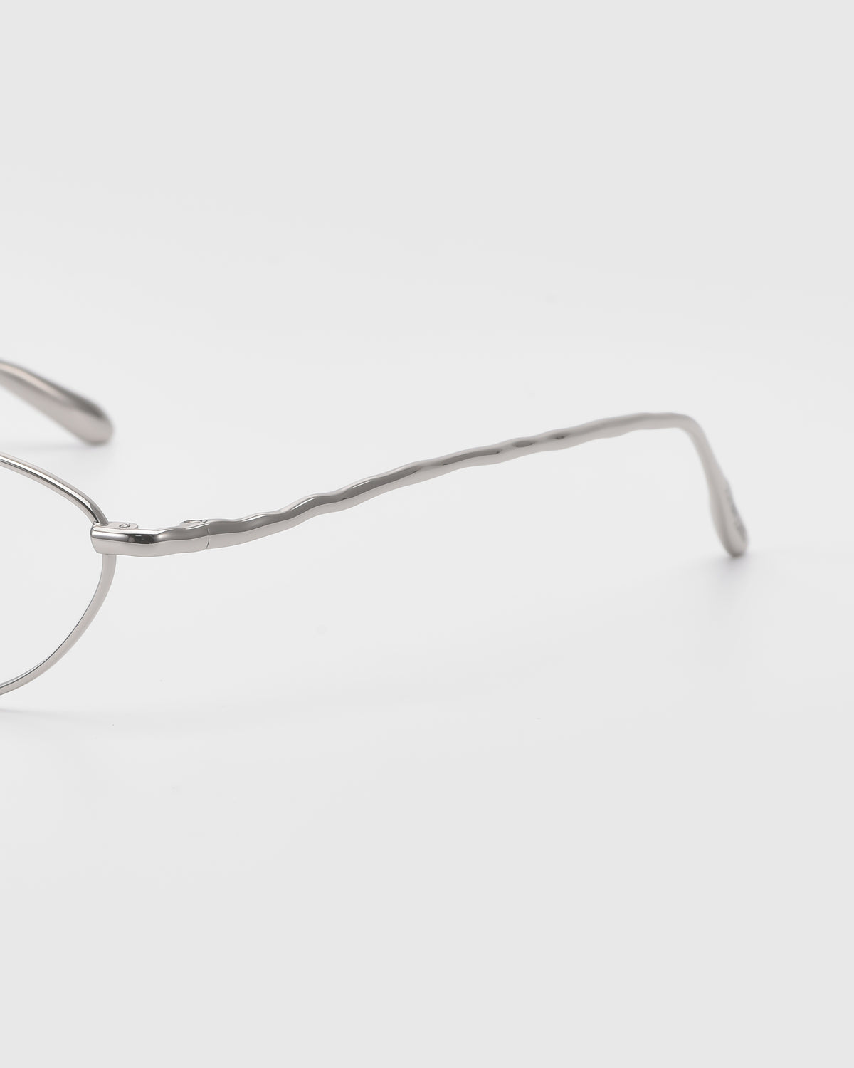 A close-up of the arm of For Art’s Sake® Suree II silver metal frames, showcasing their wavy, textured design against a plain white background.