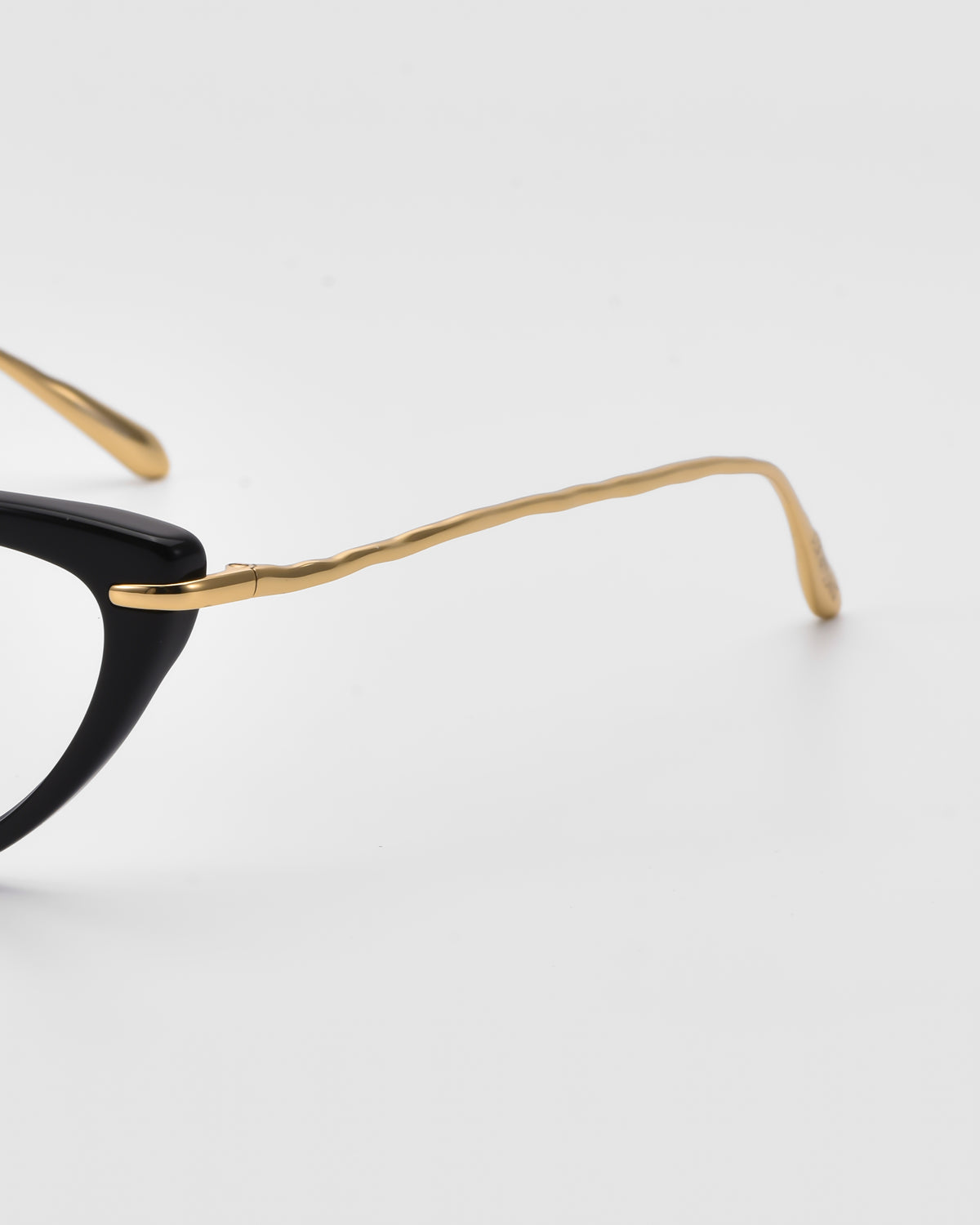 A close-up of Solange by For Art’s Sake® shows cat-eye opticals with a black frame and gold, sculpted metal temples against a plain white background.