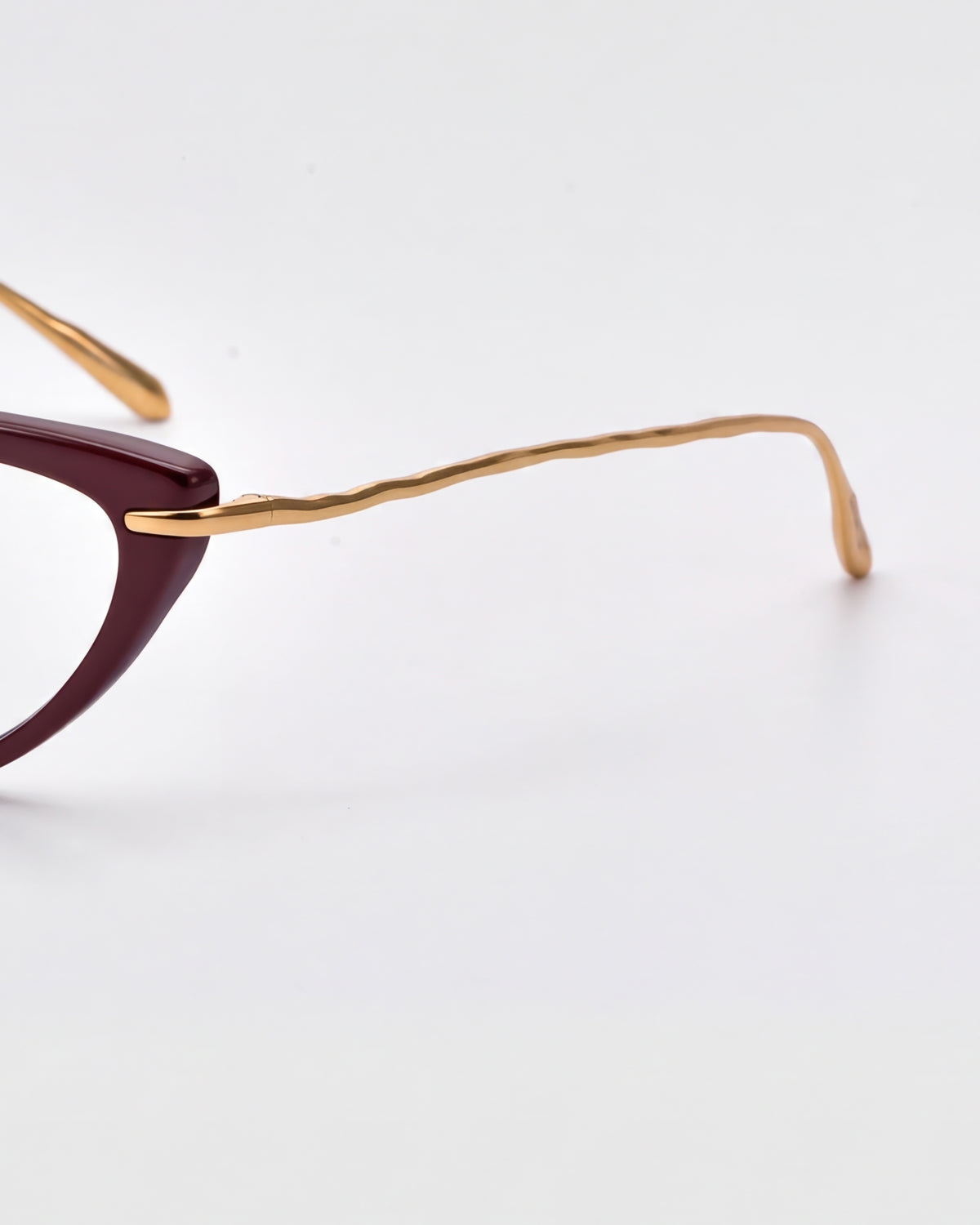 A close-up of Solange by For Art’s Sake®: cat-eye opticals with a dark purple frame and sculpted gold metal temples, set against a plain white background.