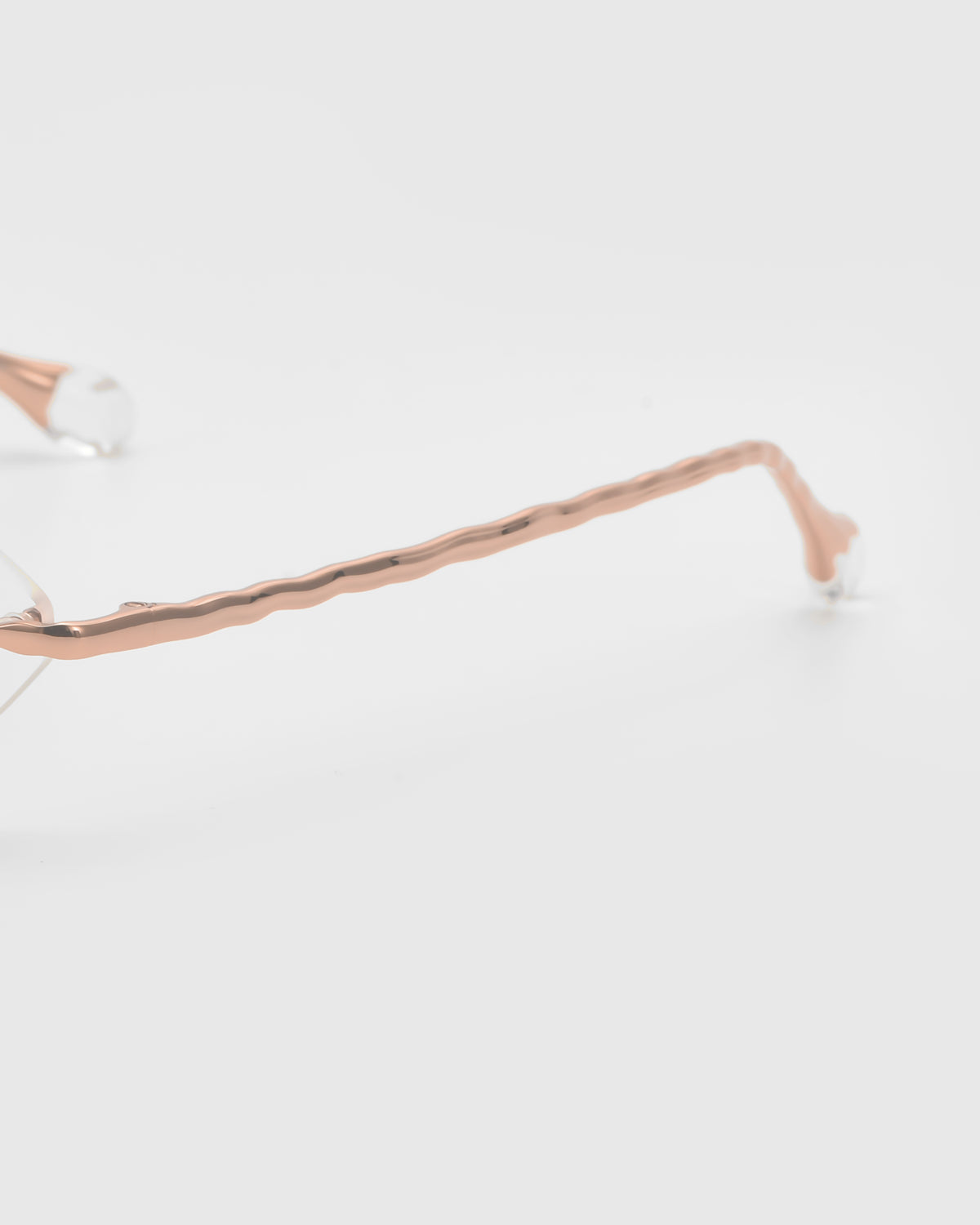 Close-up of the Amara I eyeglasses by For Art’s Sake®, showcasing a rose gold wavy arm and sculpted nylon temple tip against a plain white background.