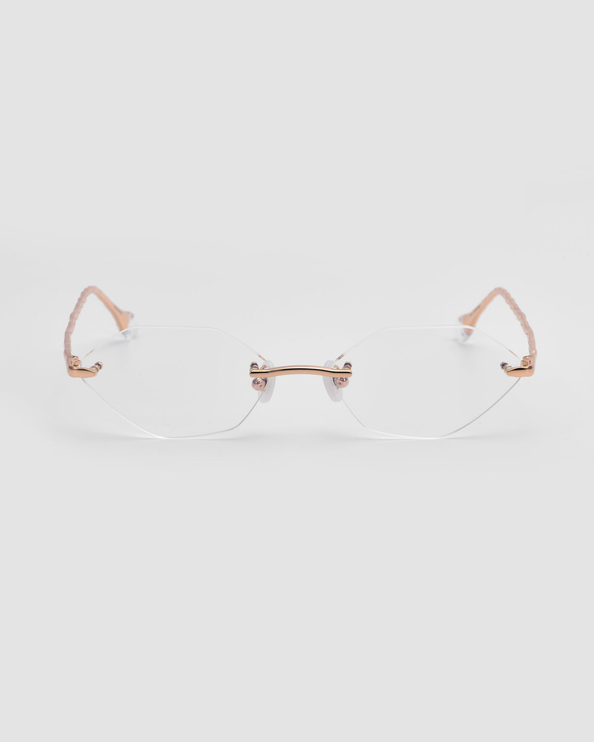 The Amara I by For Art’s Sake® features rimless optical frames, clear lenses, rose gold arms, and sculpted nylon temple tips, shown on a plain light gray background.