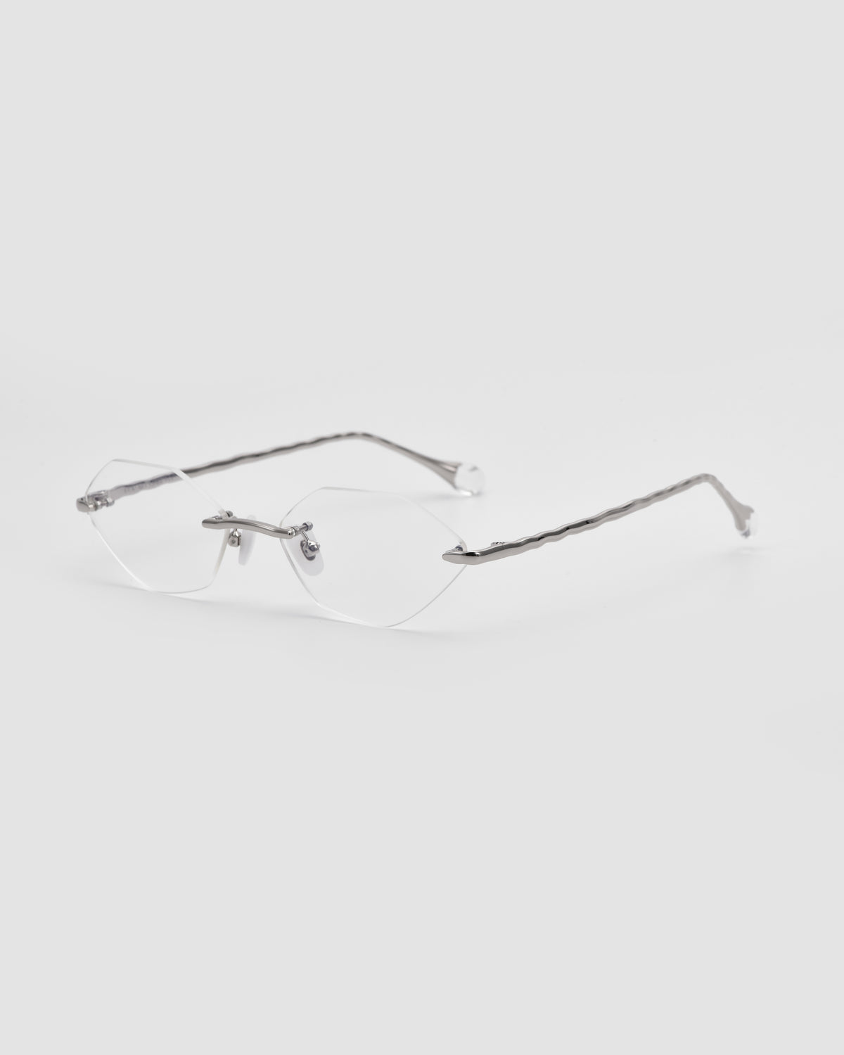 The Amara I by For Art’s Sake®: rimless eyeglasses with clear lenses, silver metal arms, and sculpted nylon temple tips, shown on a light gray background.