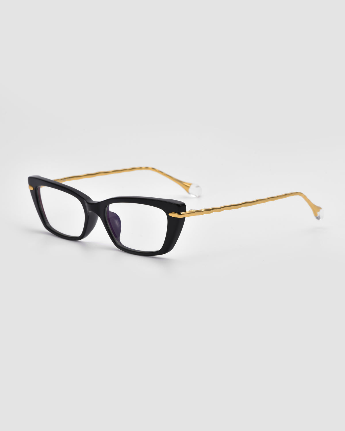The Amara II by For Art’s Sake® features black square optical frames with thick rims, gold wavy metal arms, and sculpted nylon temple tips, shown on a plain white background.