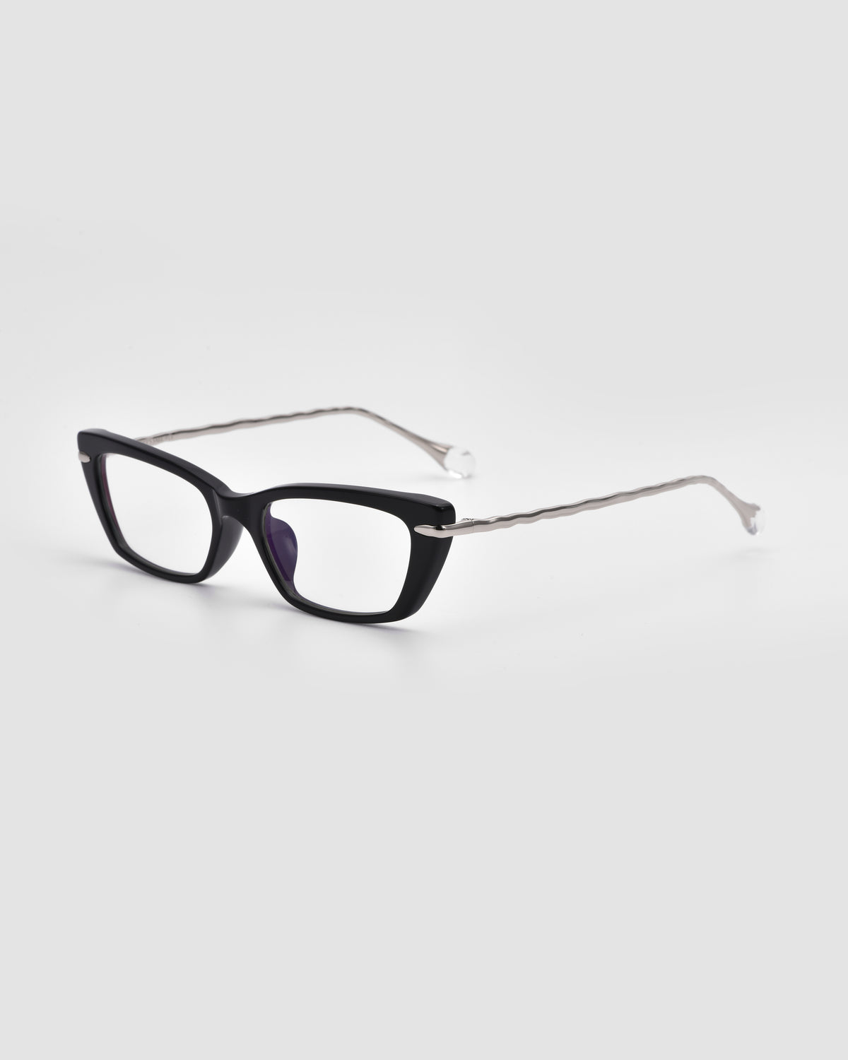 The Amara II by For Art’s Sake® features black rectangular optical frames with thick fronts, thin silver wavy arms, and sculpted nylon temple tips, set against a plain light gray background.