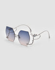 Rimless sunglasses with a silver metal frame and gradient lenses that fade from blue at the top to a soft pink at the bottom, shown on a light gray background.