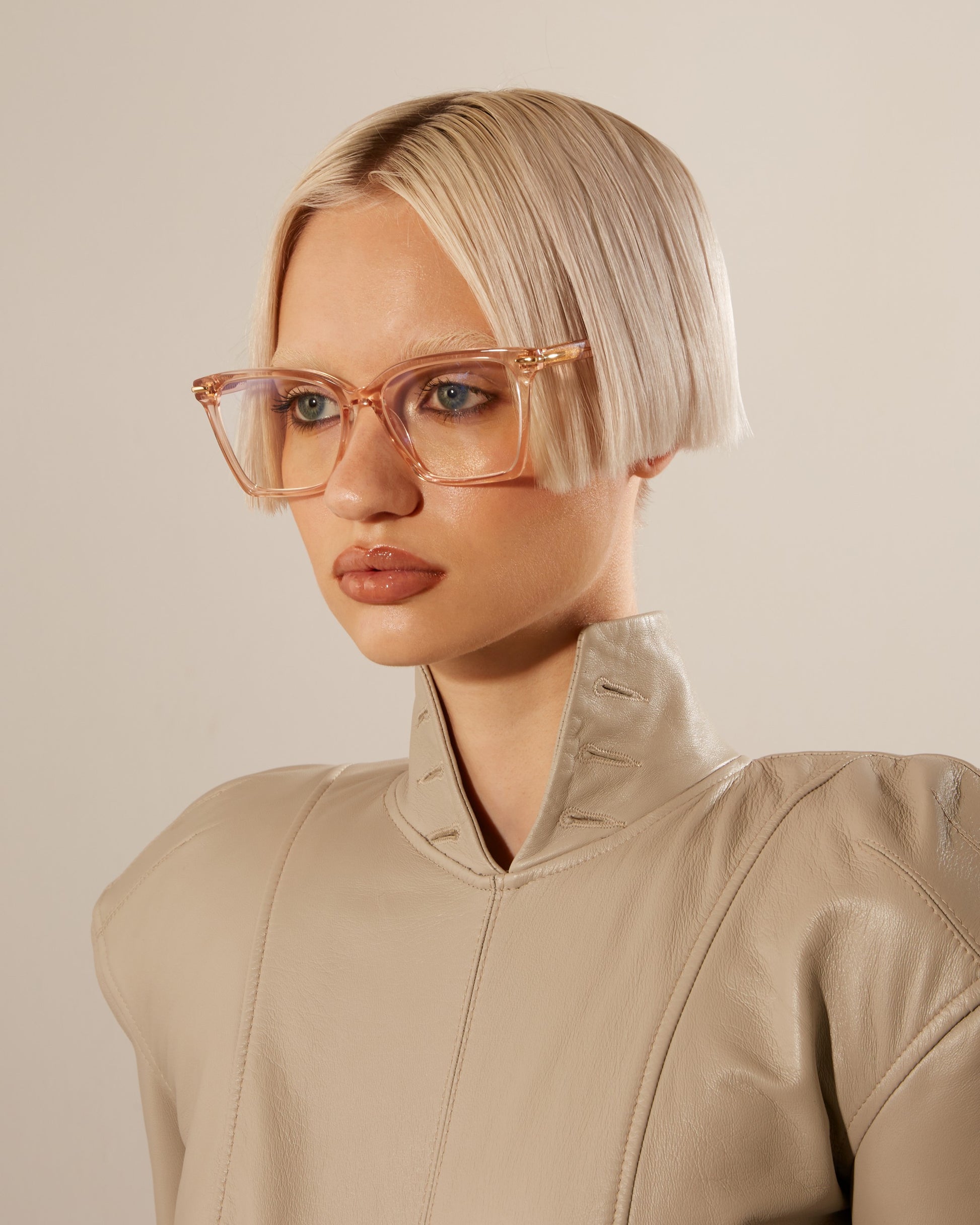 A woman with short straight blonde hair and clear-frame pink optical glasses.